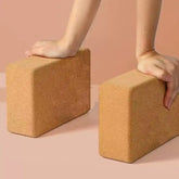 Two cork yoga blocks being held by hands on a beige background
